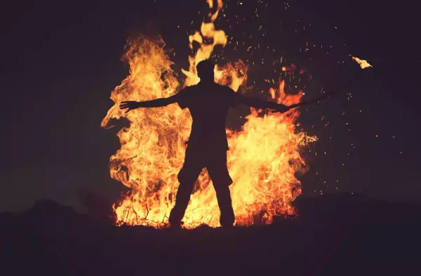 Men standing in front of a big fire with a torch on fire in his hand