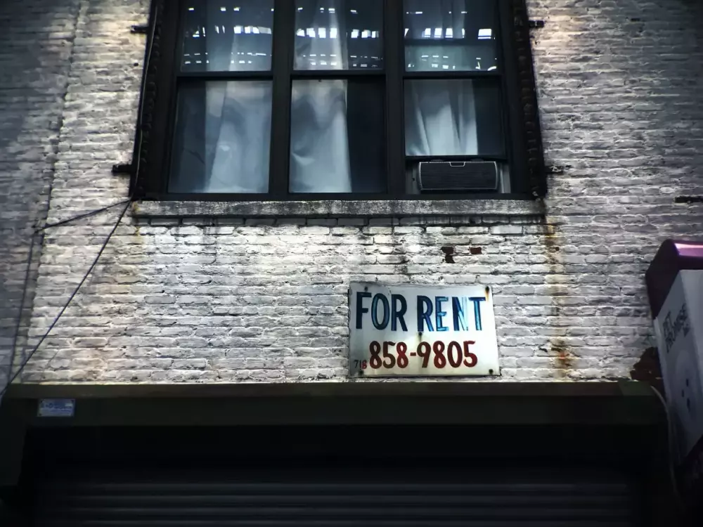 For rent sign below a window of a brick building.